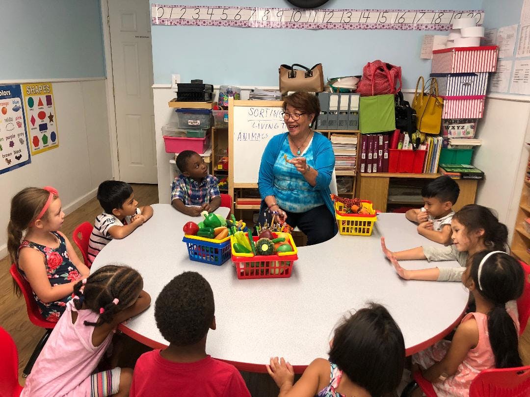 Adult teaching children at a round table with toy food baskets