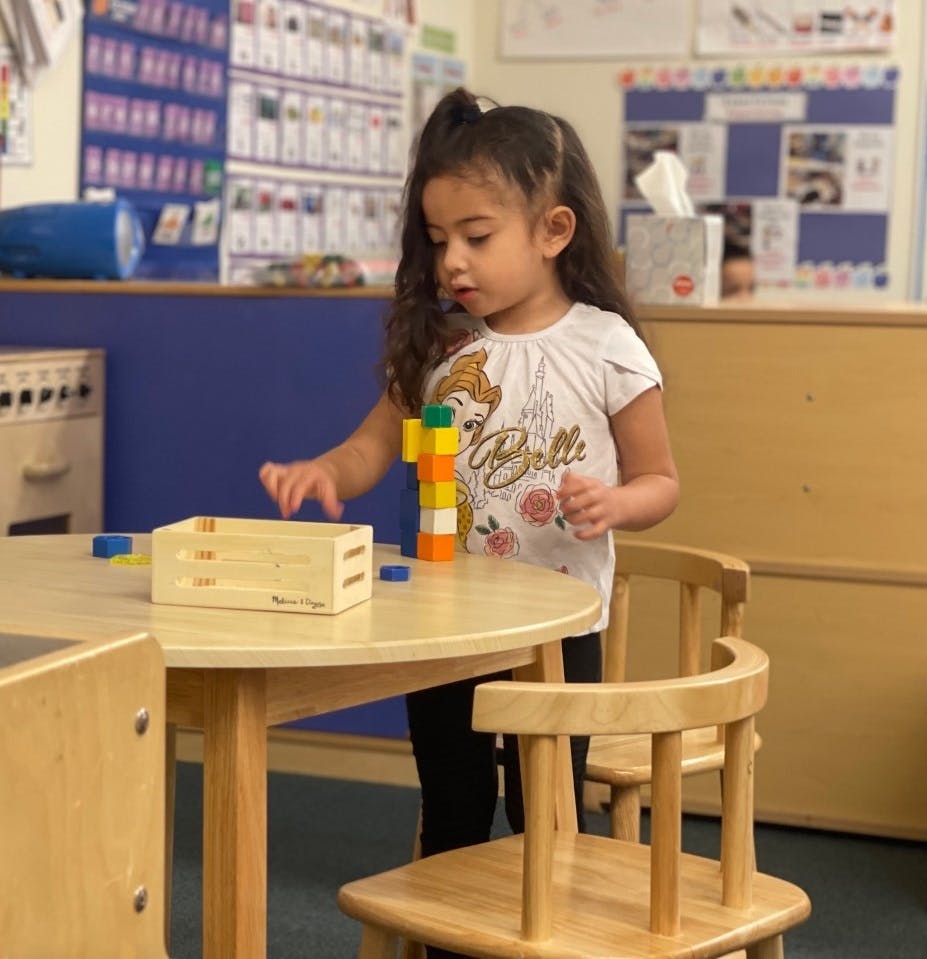 Child playing with colorful building blocks at a table in a classroom