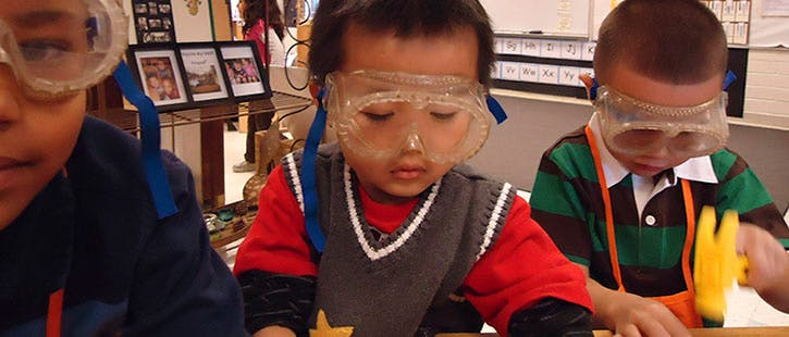 Three children wearing safety goggles in a classroom