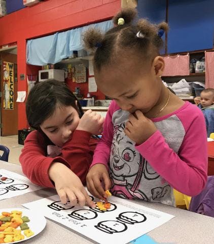 Two children playing with small objects on a paper with drawings