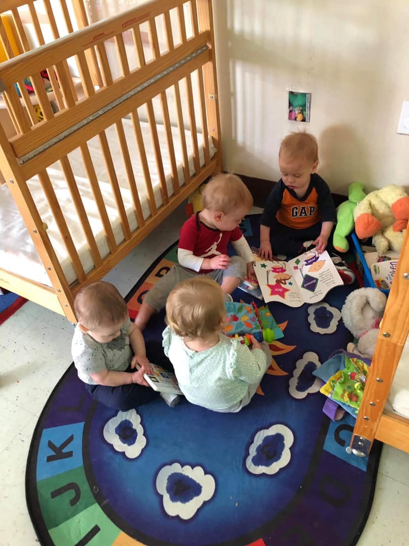 Four children sitting on a rug with books and toys