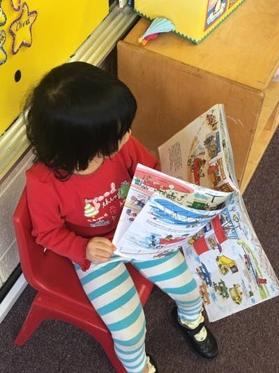 Child sitting on a red chair and looking at a book