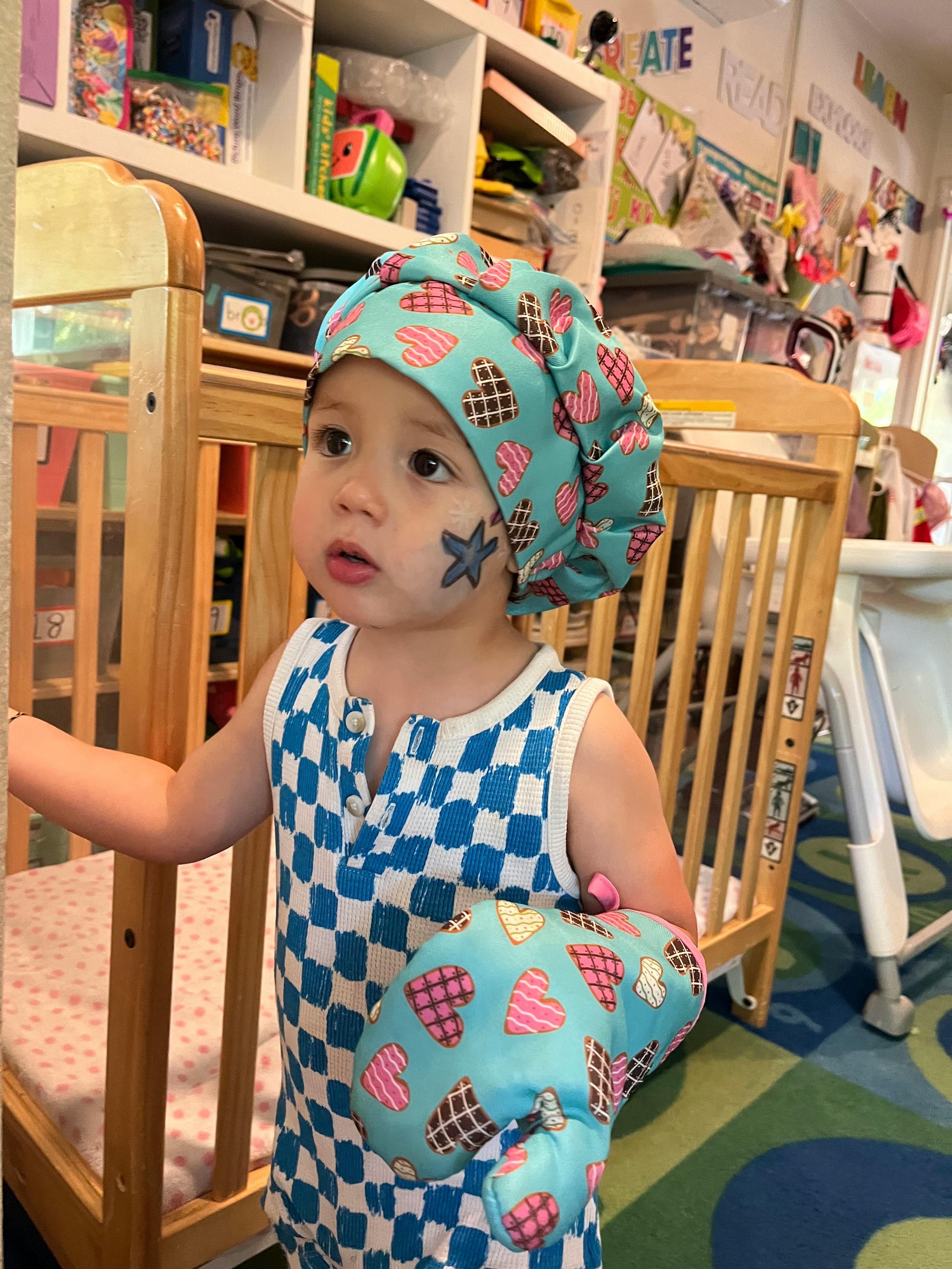 Child wearing a chef's hat and oven mitt, with a star painted on their cheek