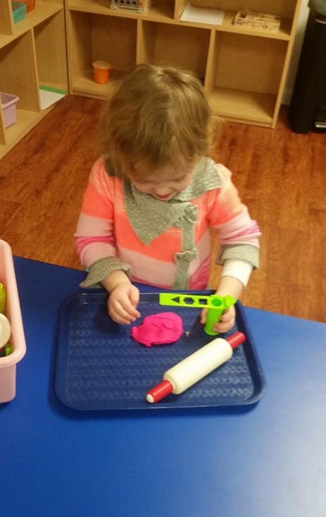 Child playing with pink playdough and a rolling pin on a blue tray