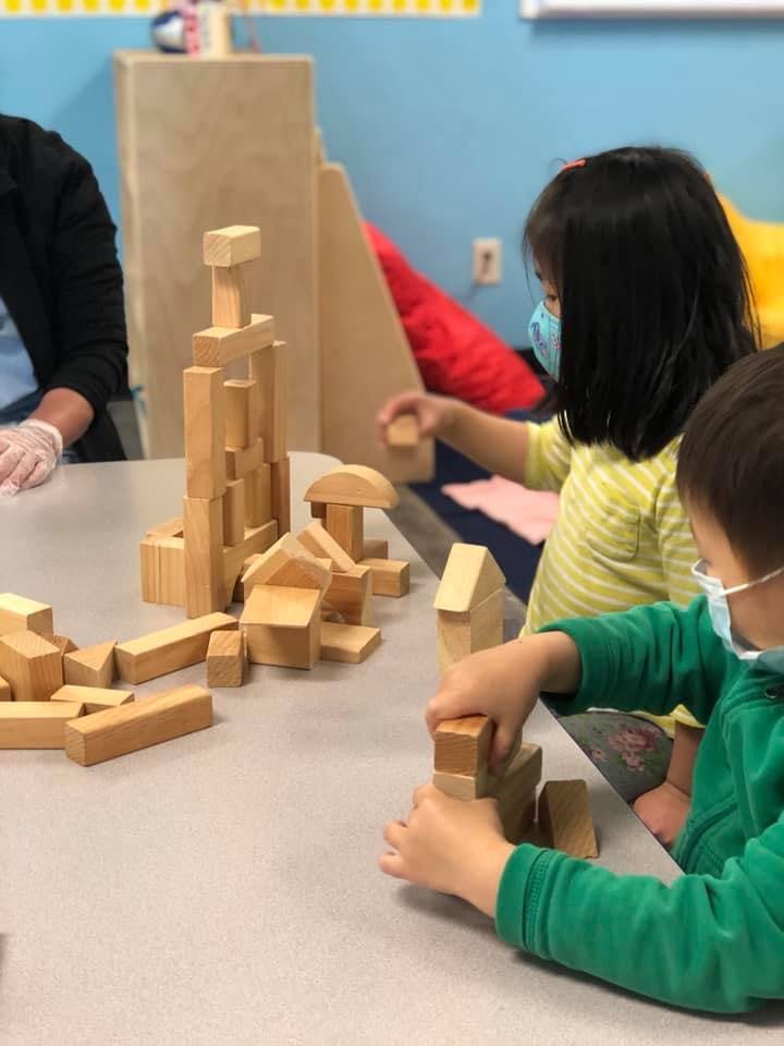 Two children in masks playing with wooden blocks at a table