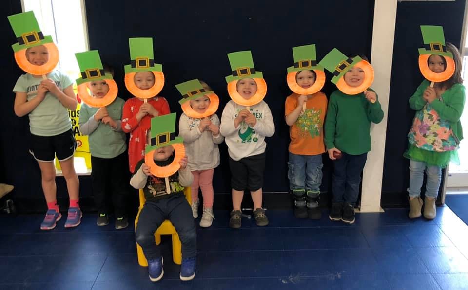Children holding up paper leprechaun hats covering their faces