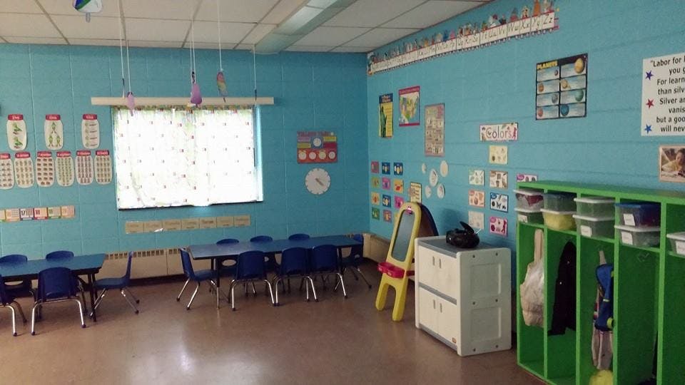 Classroom with blue walls, small tables, and green storage shelves