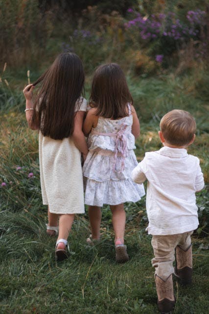 Three children walking away through a grassy field