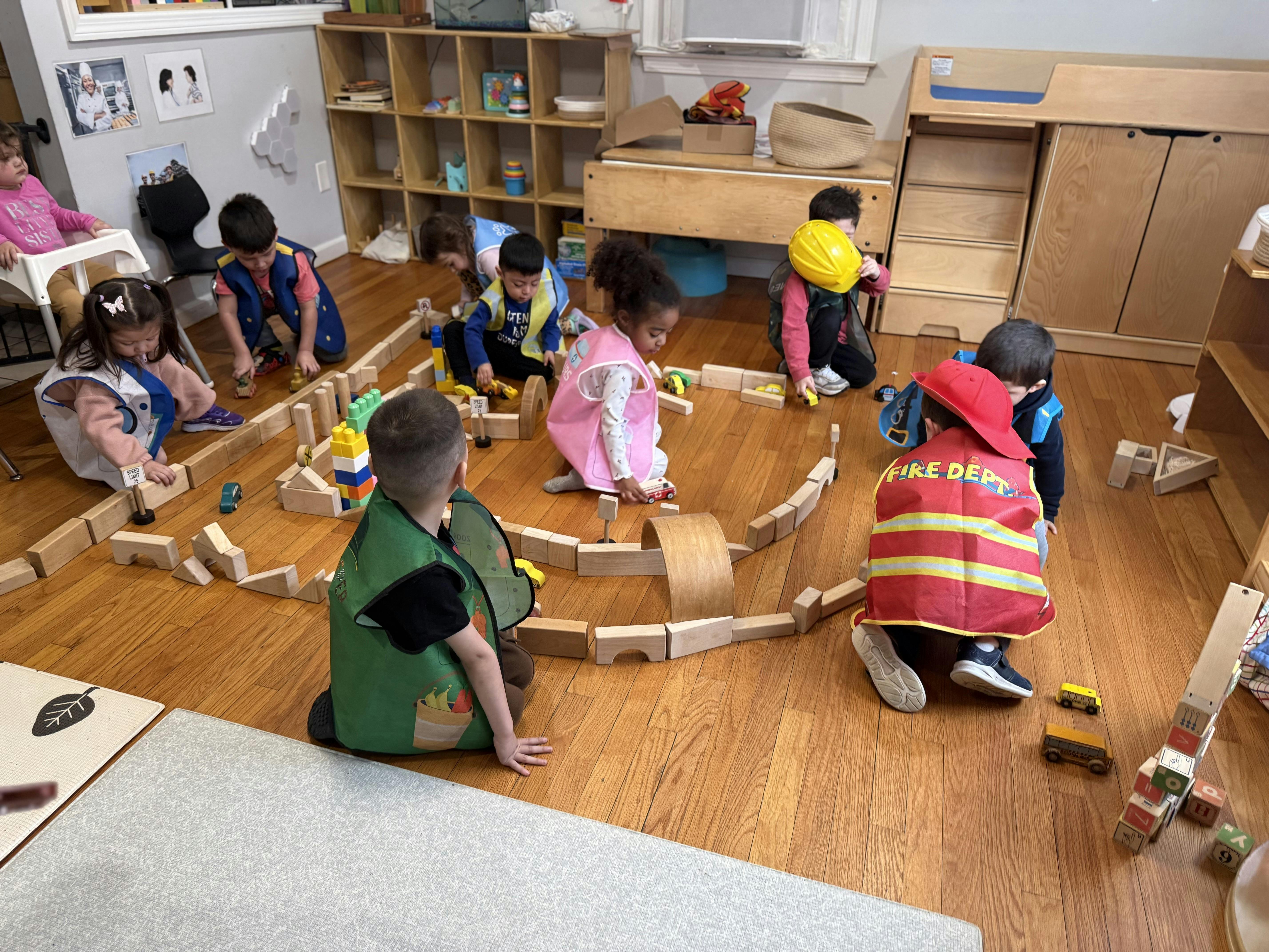 Children wearing play vests playing with wooden blocks and toy cars on the floor