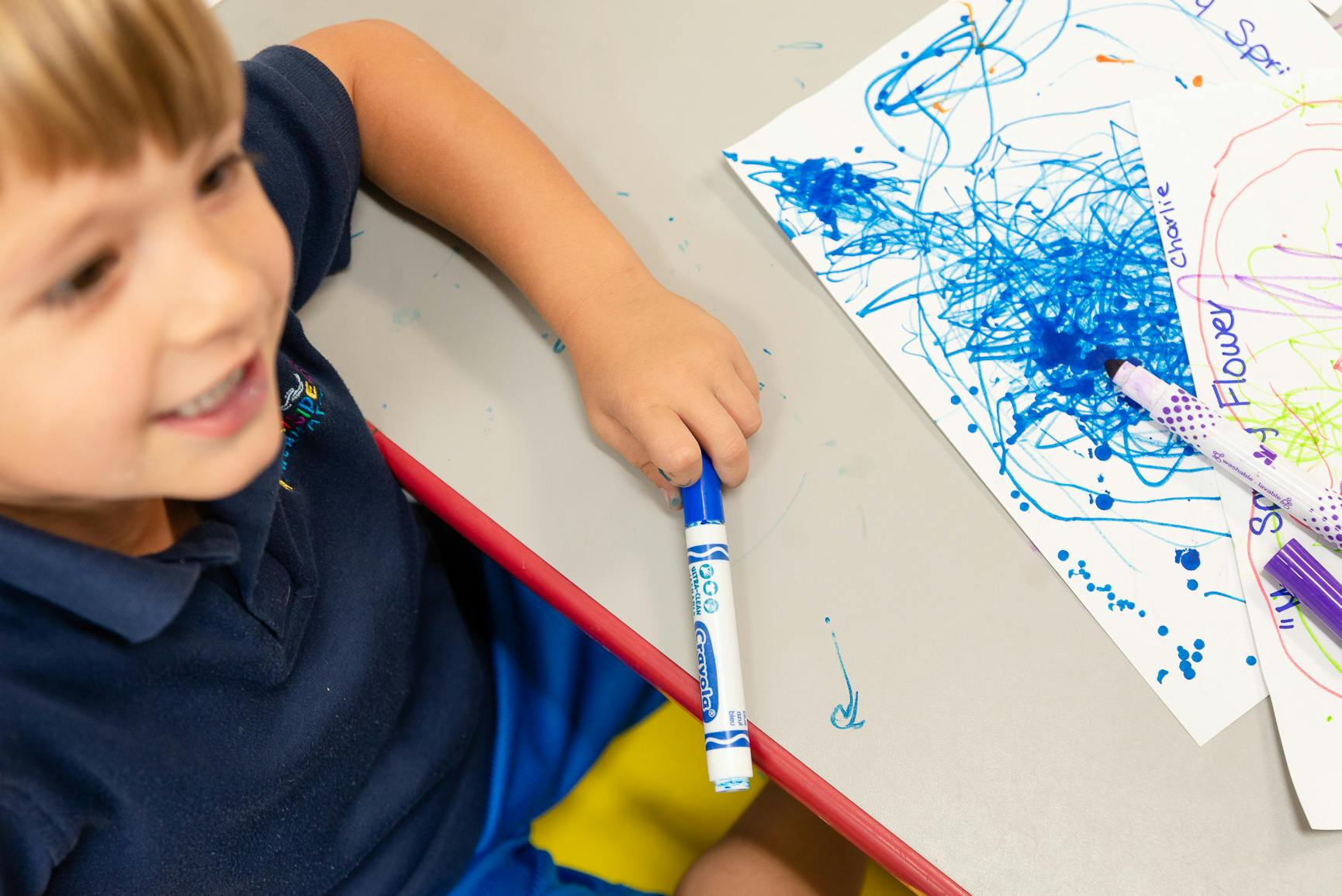 Child holding a blue marker over a paper with blue scribbles