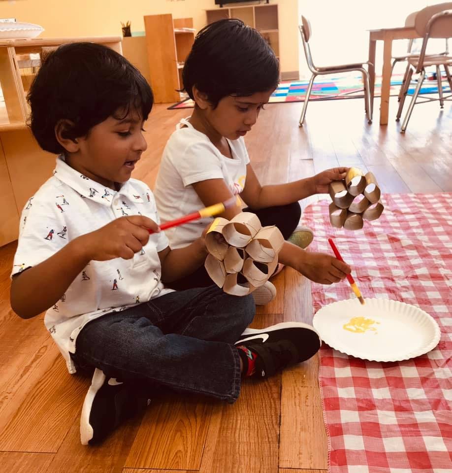 Two children painting paper tube crafts on a red and white checkered mat