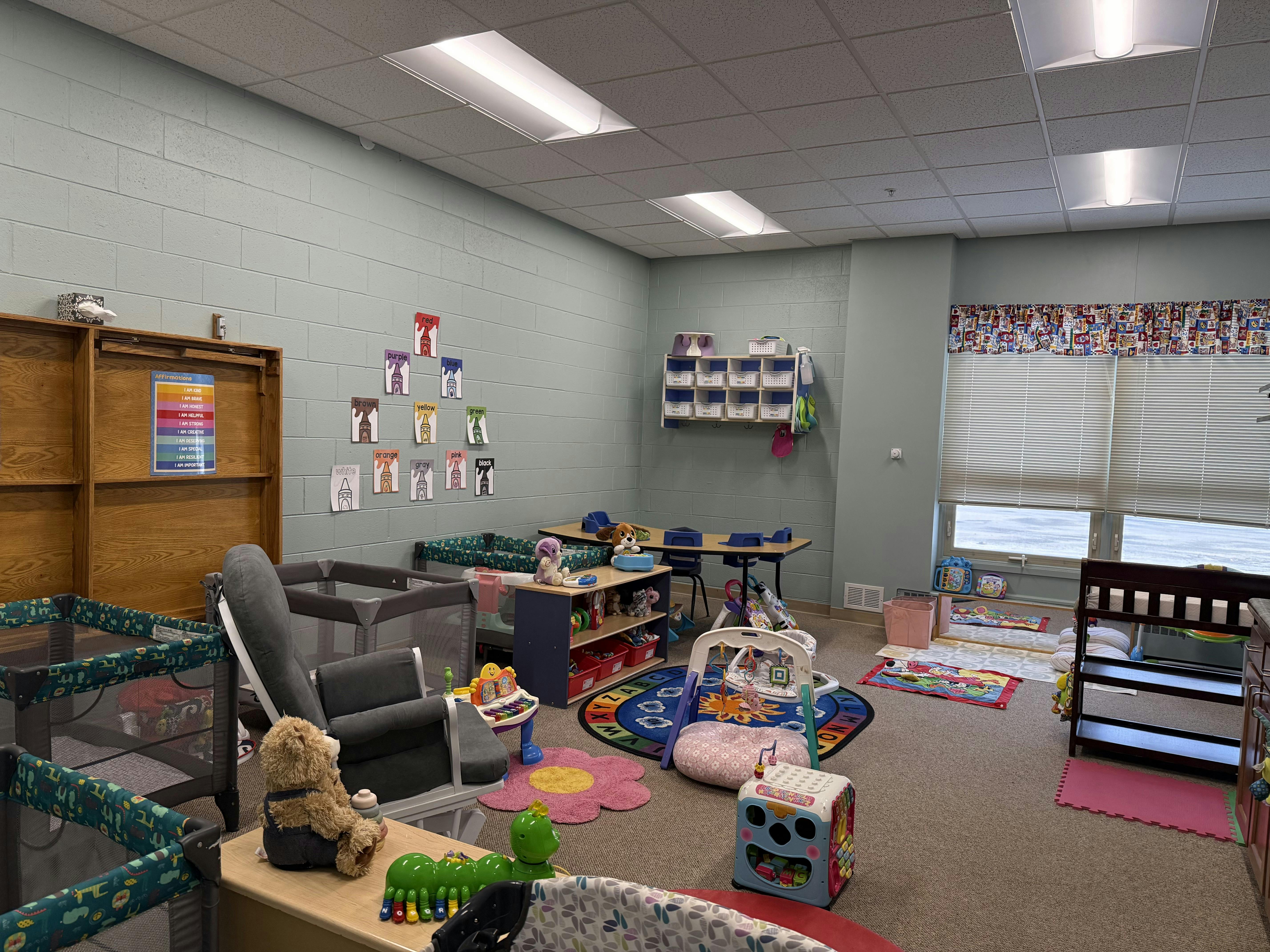 Baby and toddler daycare room with playards, crib, and various toys