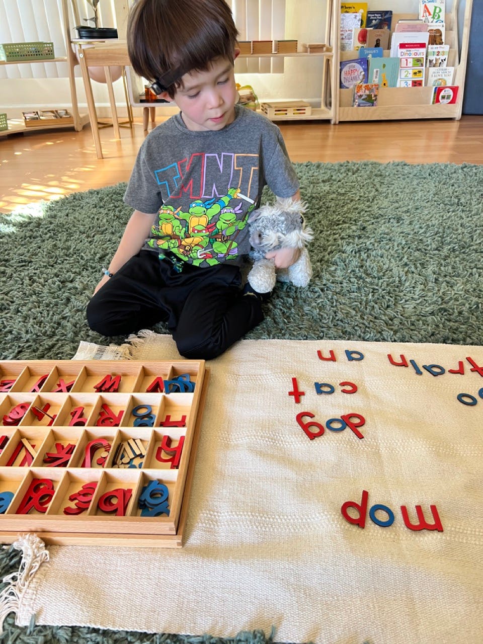 Child on floor with toy, wooden letter tray, and words spelled out