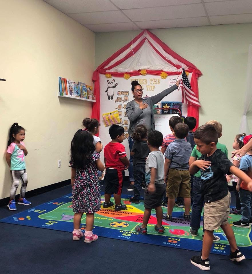 Adult and children standing with hands over hearts, facing American flag