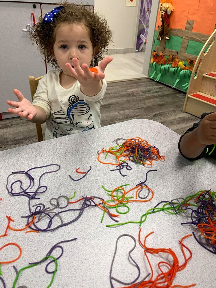 Child holding a small orange object over a table with colorful yarn