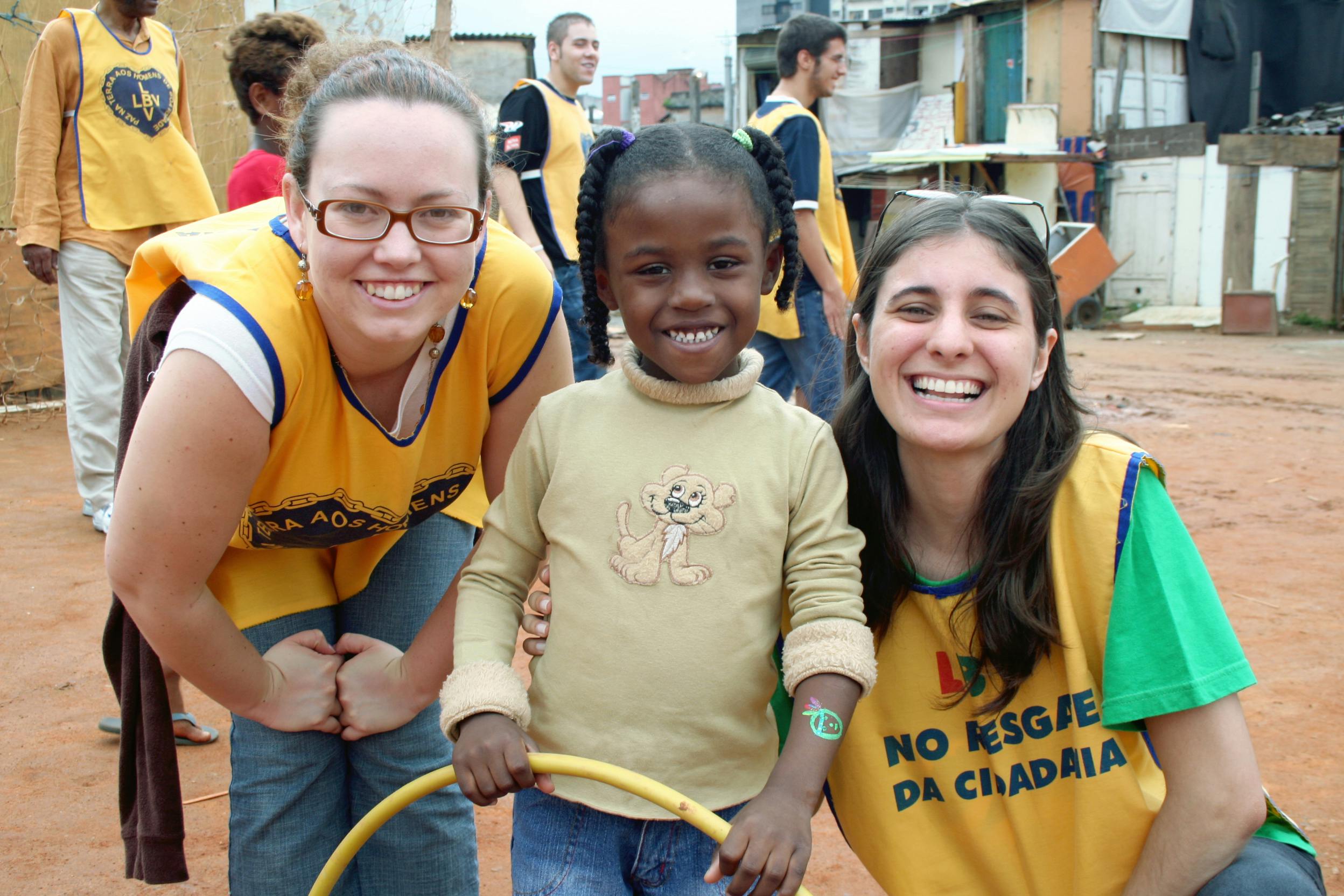 Two smiling women in yellow vests with a child holding a yellow hoop