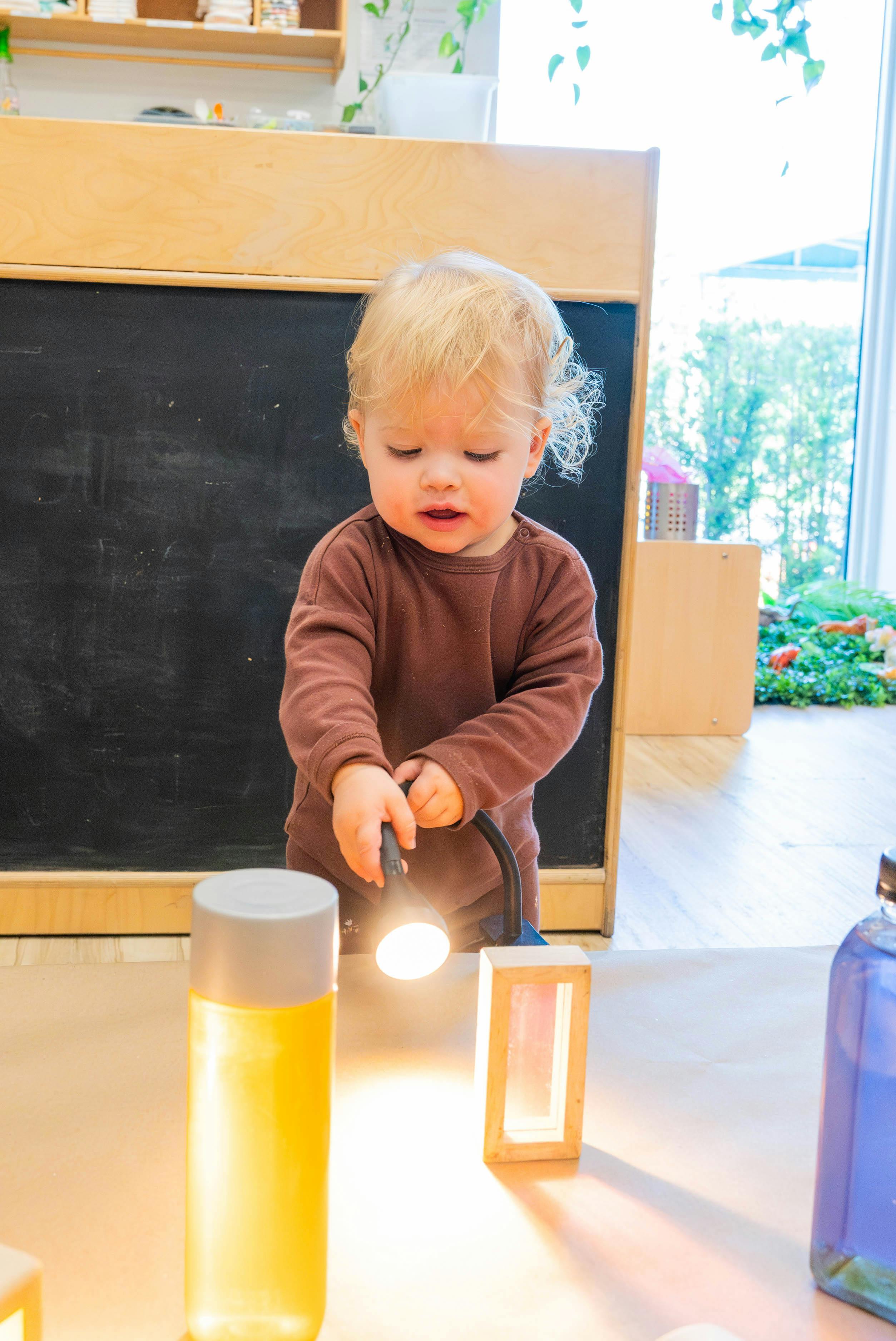 Child holding a clamp lamp, shining it on a table with light-up objects