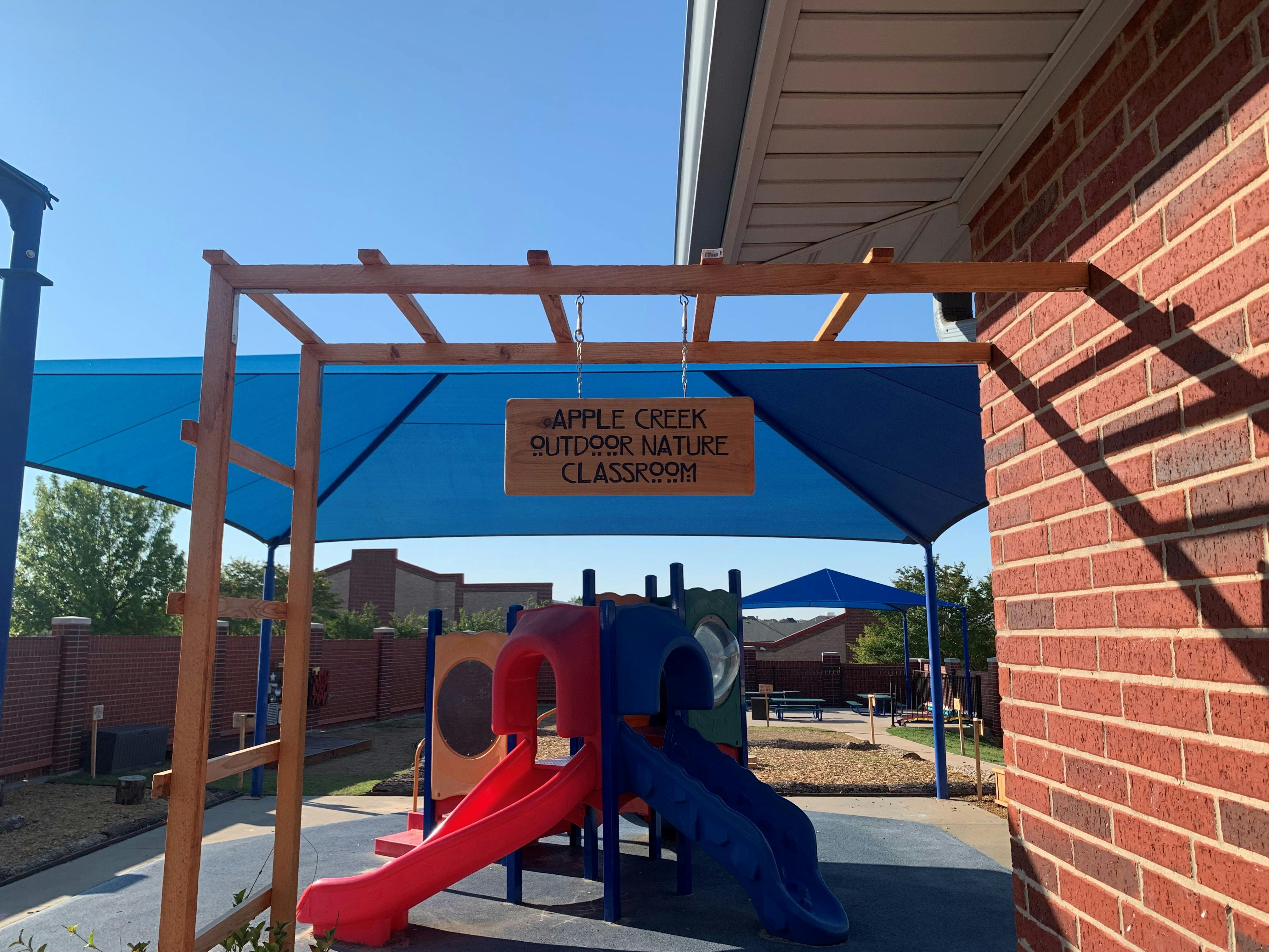 Playground with a red and blue slide under a blue shade structure and brown shade structure