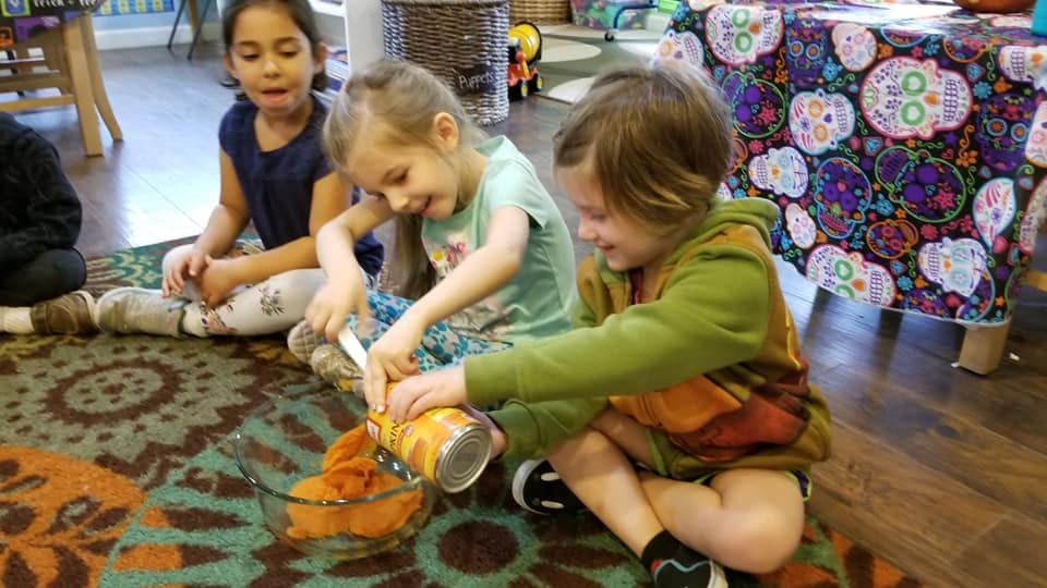 Children sitting on a rug, one child holding a container