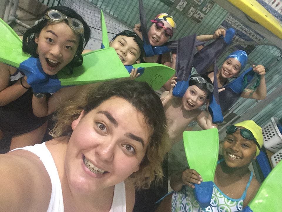 Person taking a selfie with multiple children wearing swim gear and holding fins