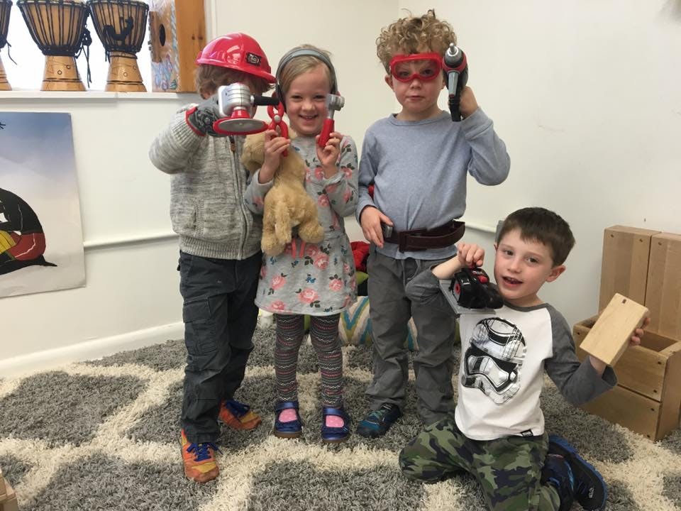 Four children playing with toy tools and dress-up items