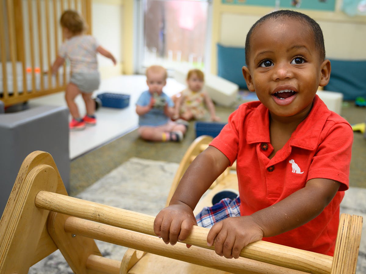 Child in red shirt holding onto wooden play equipment