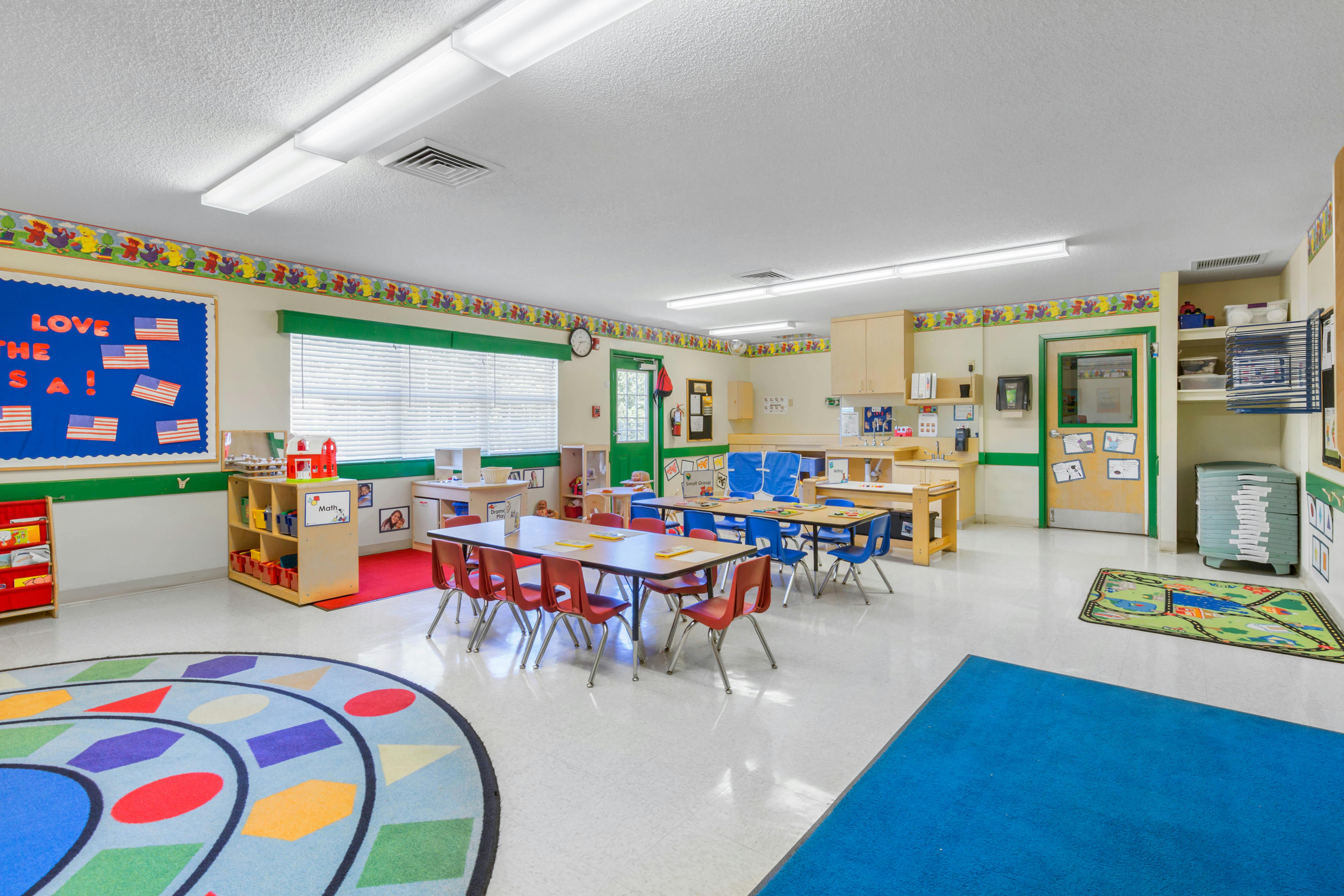 An empty classroom with small tables, chairs, and learning materials