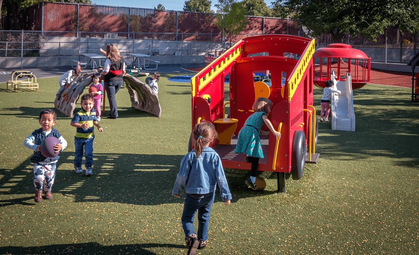 Children playing on a playground with a red play structure