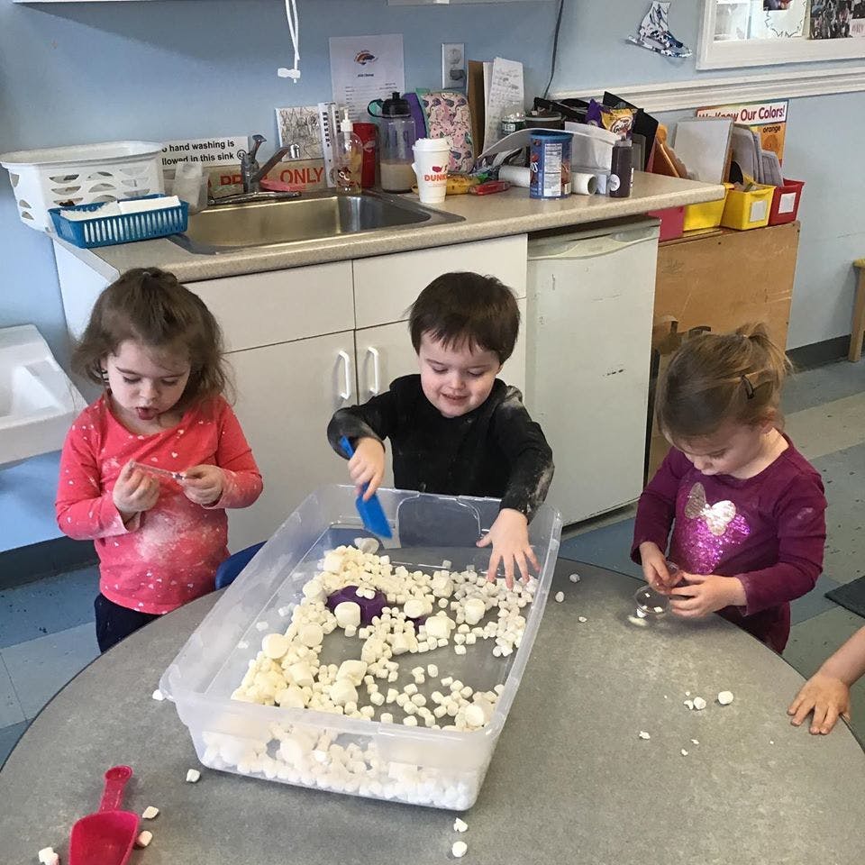 Three children playing with white foam pieces in a classroom