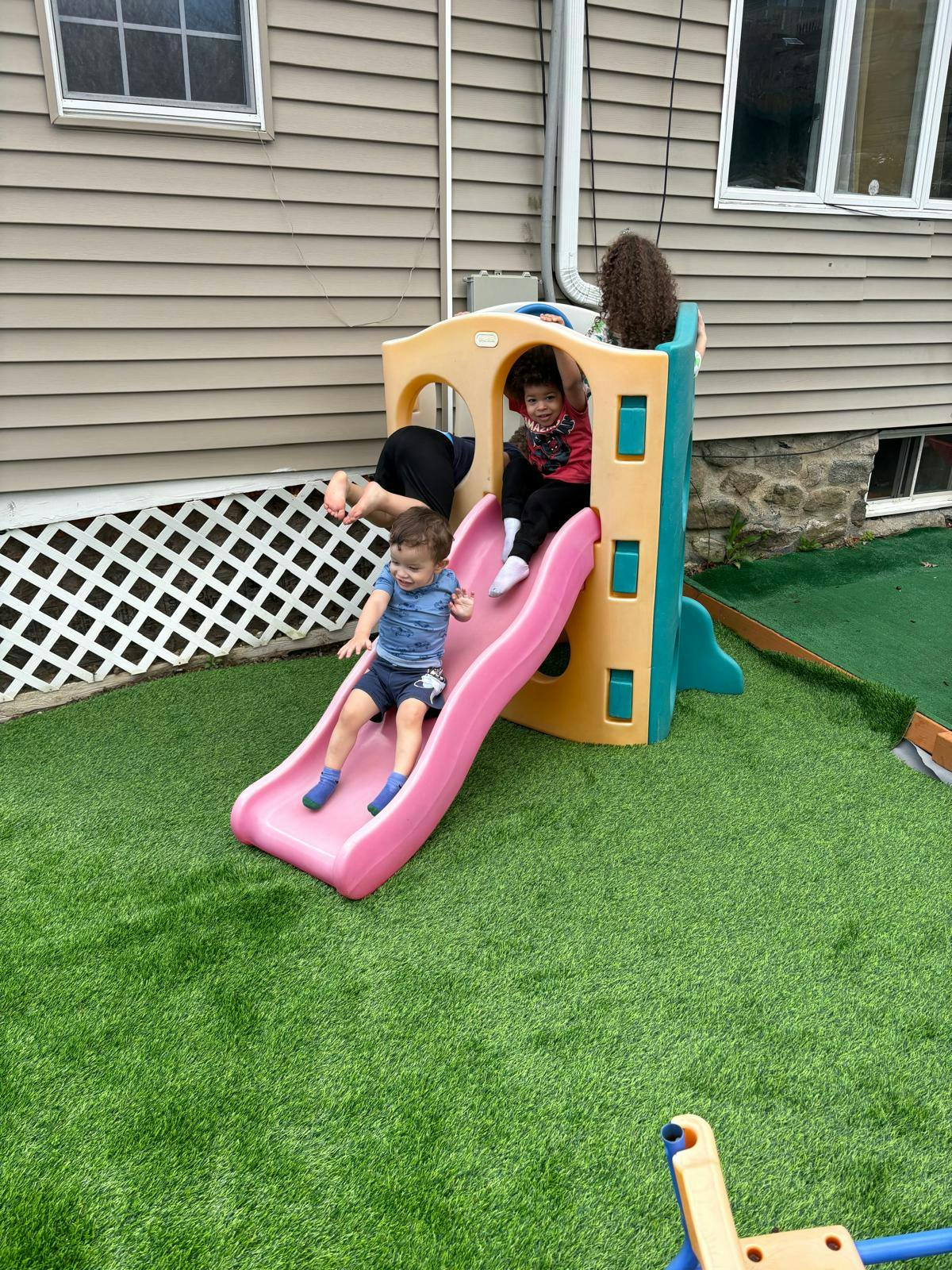 Child sliding down a pink slide as another child sits at the top