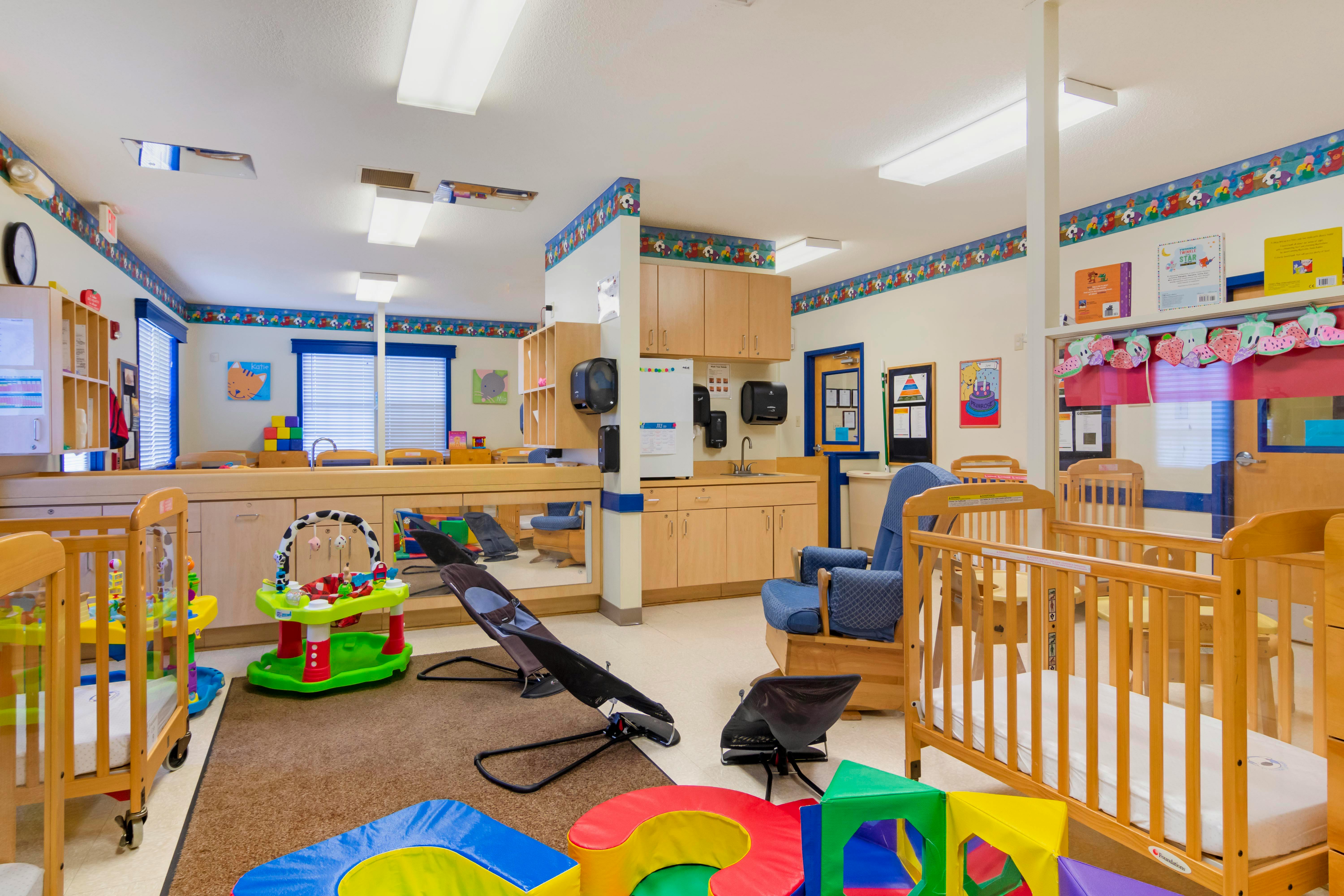Cribs, infant bouncer seats, and soft play blocks in a daycare room