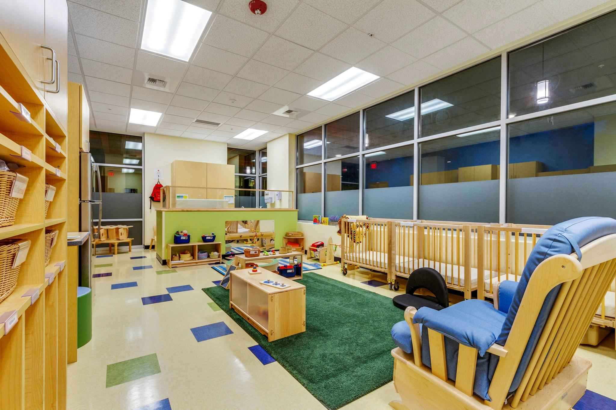Daycare room with cribs, play area, and rocking chair