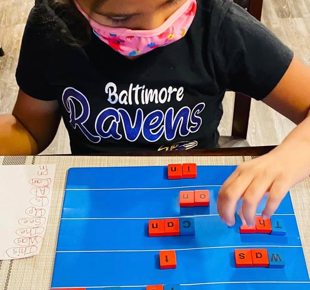 Child in a mask playing with letter tiles on a blue board