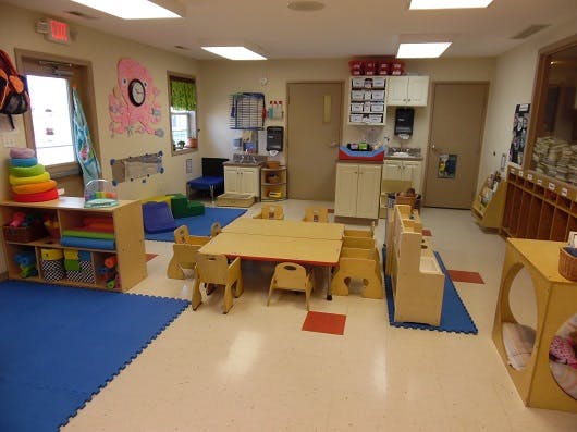 Classroom with small tables and chairs, blue mats, and storage shelves