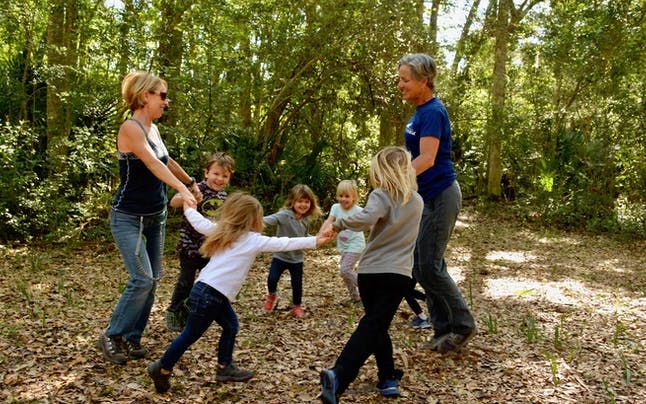 Two adults and four children holding hands in a circle outdoors