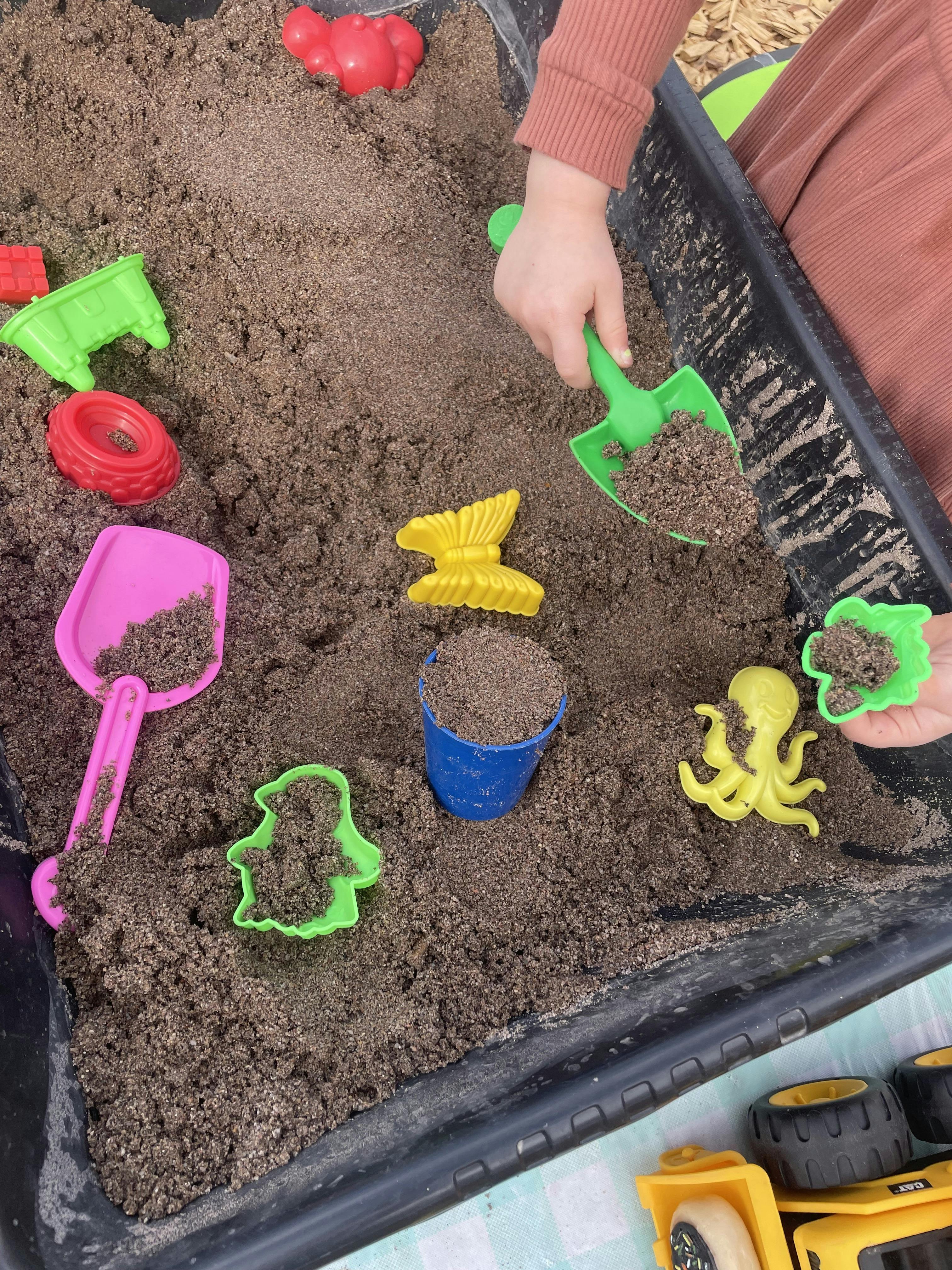 Child playing with plastic molds and a shovel in a sand table