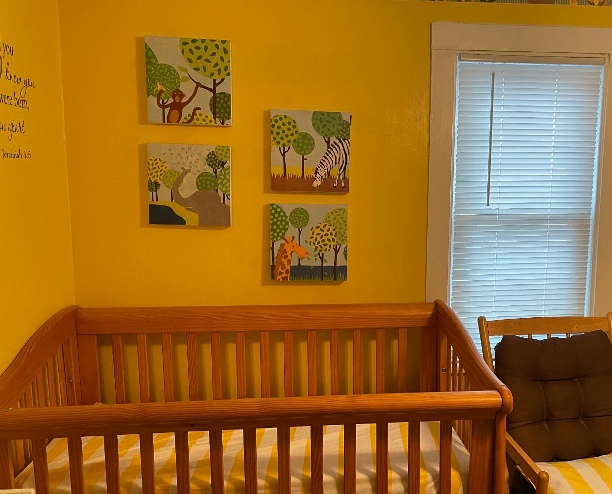Wooden crib in a room with yellow walls and animal-themed wall art