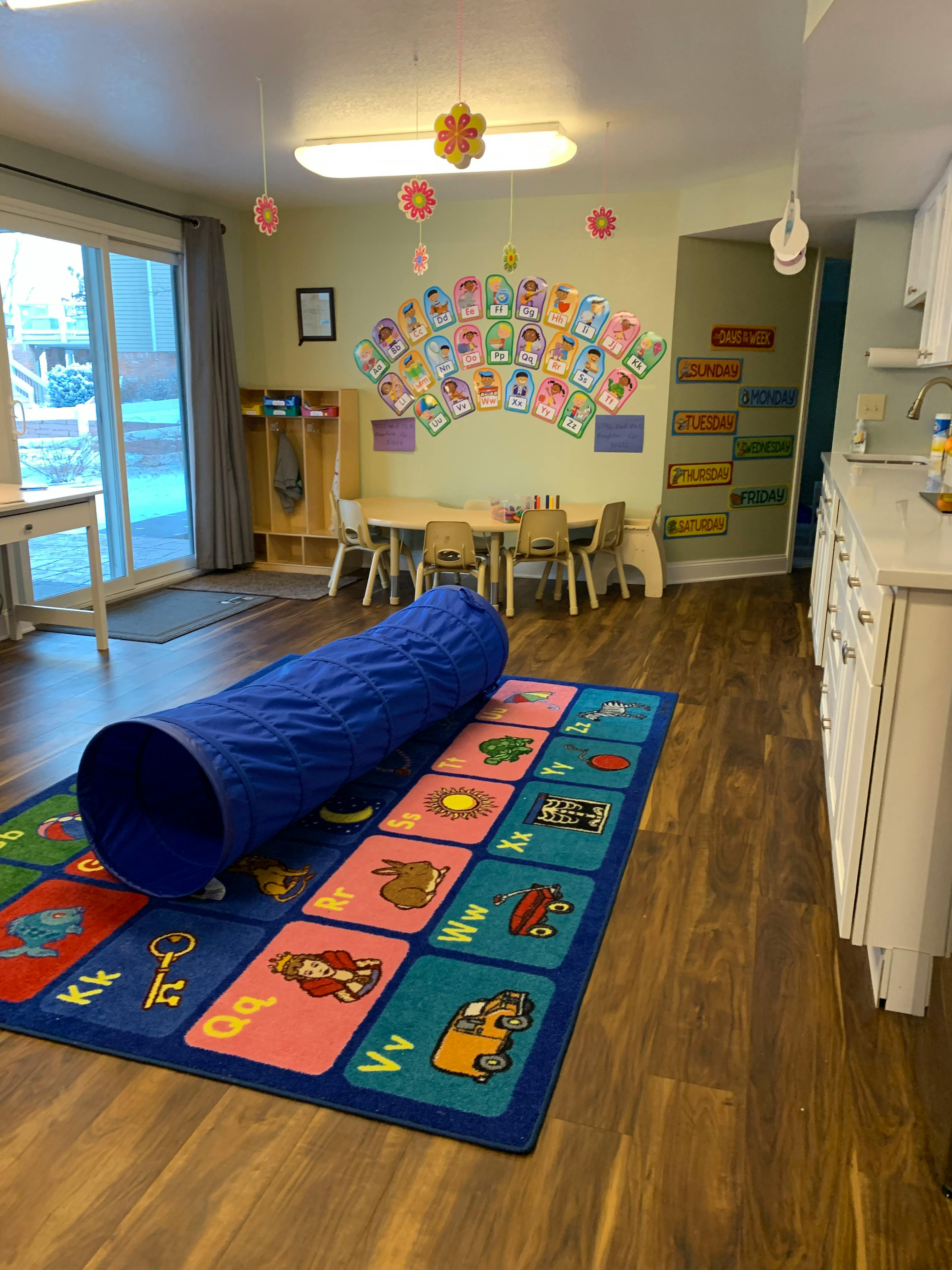 Playroom with a blue tunnel on an alphabet rug, small table and chairs