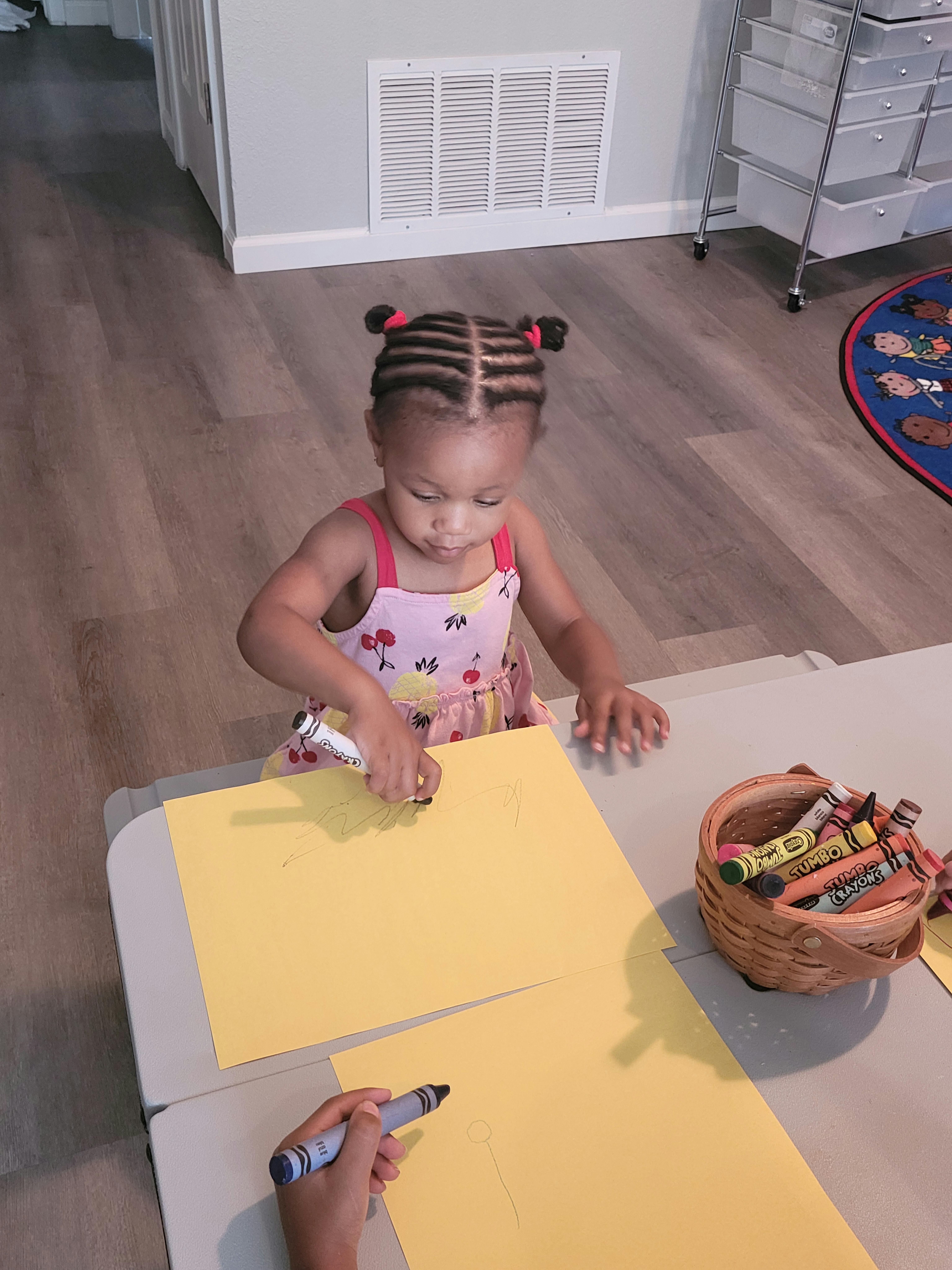 Child drawing on yellow paper with a crayon