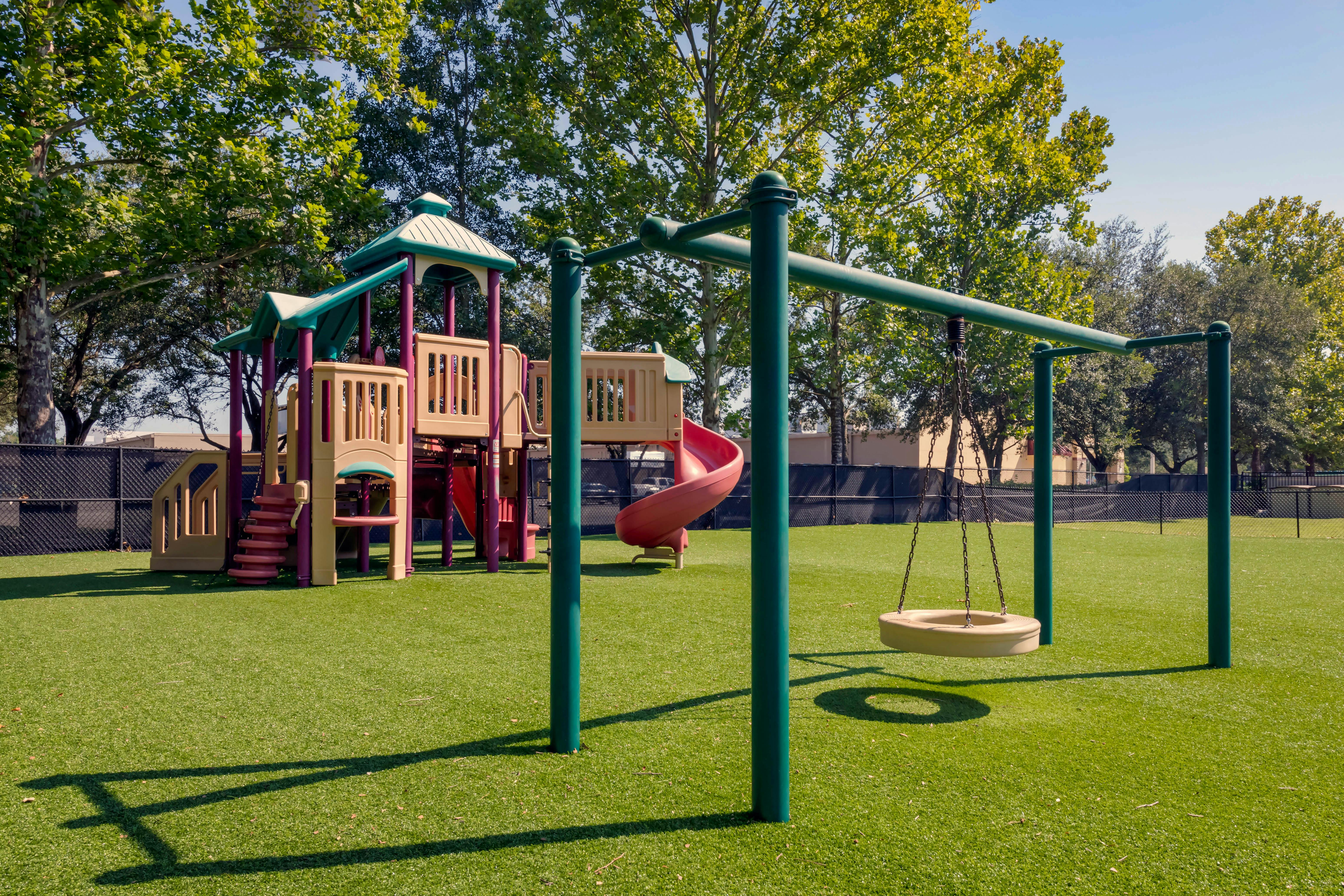 Playground with swings, slides, and climbing structures on green artificial turf