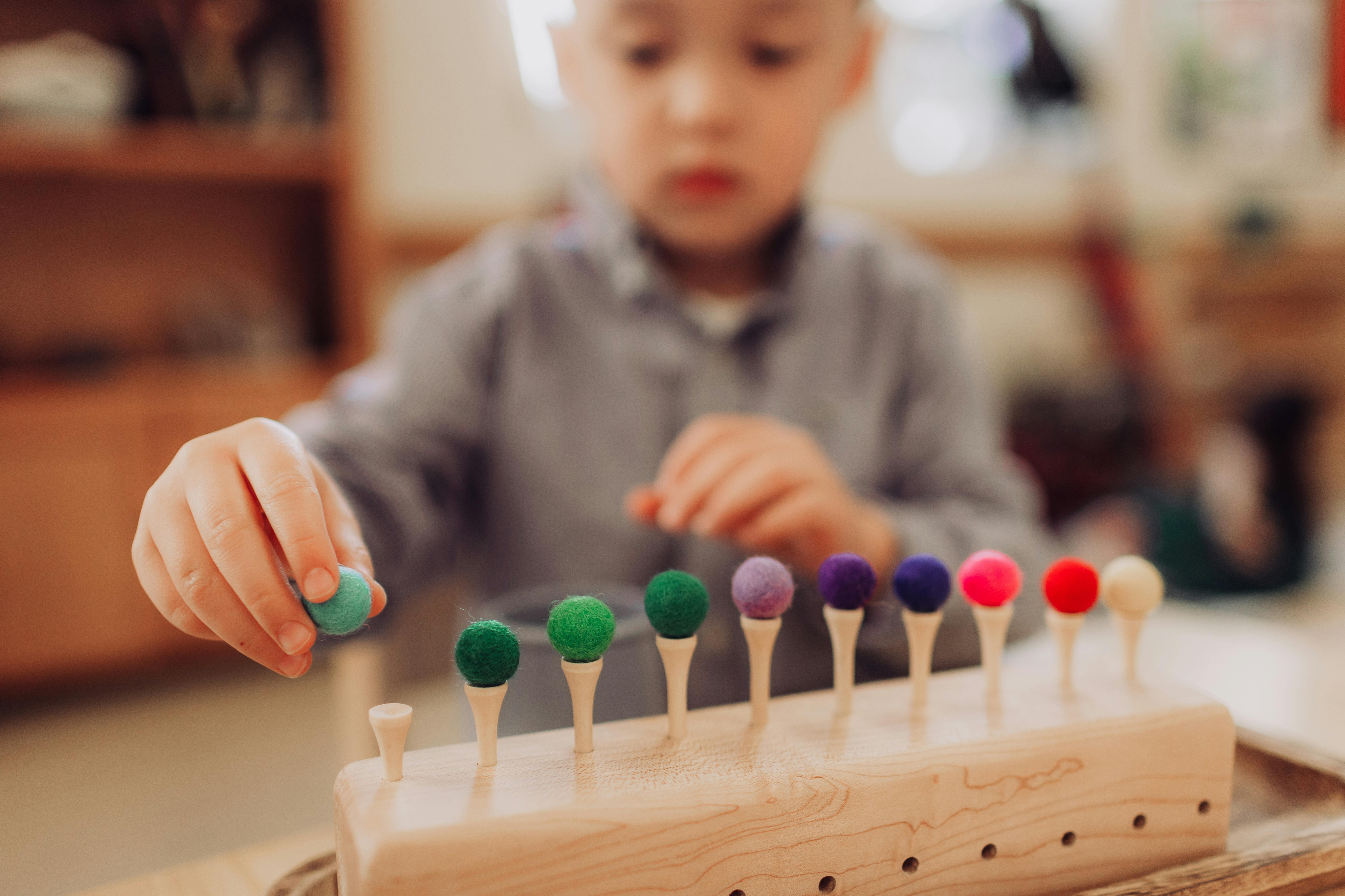 Child placing a pom-pom on a wooden peg toy