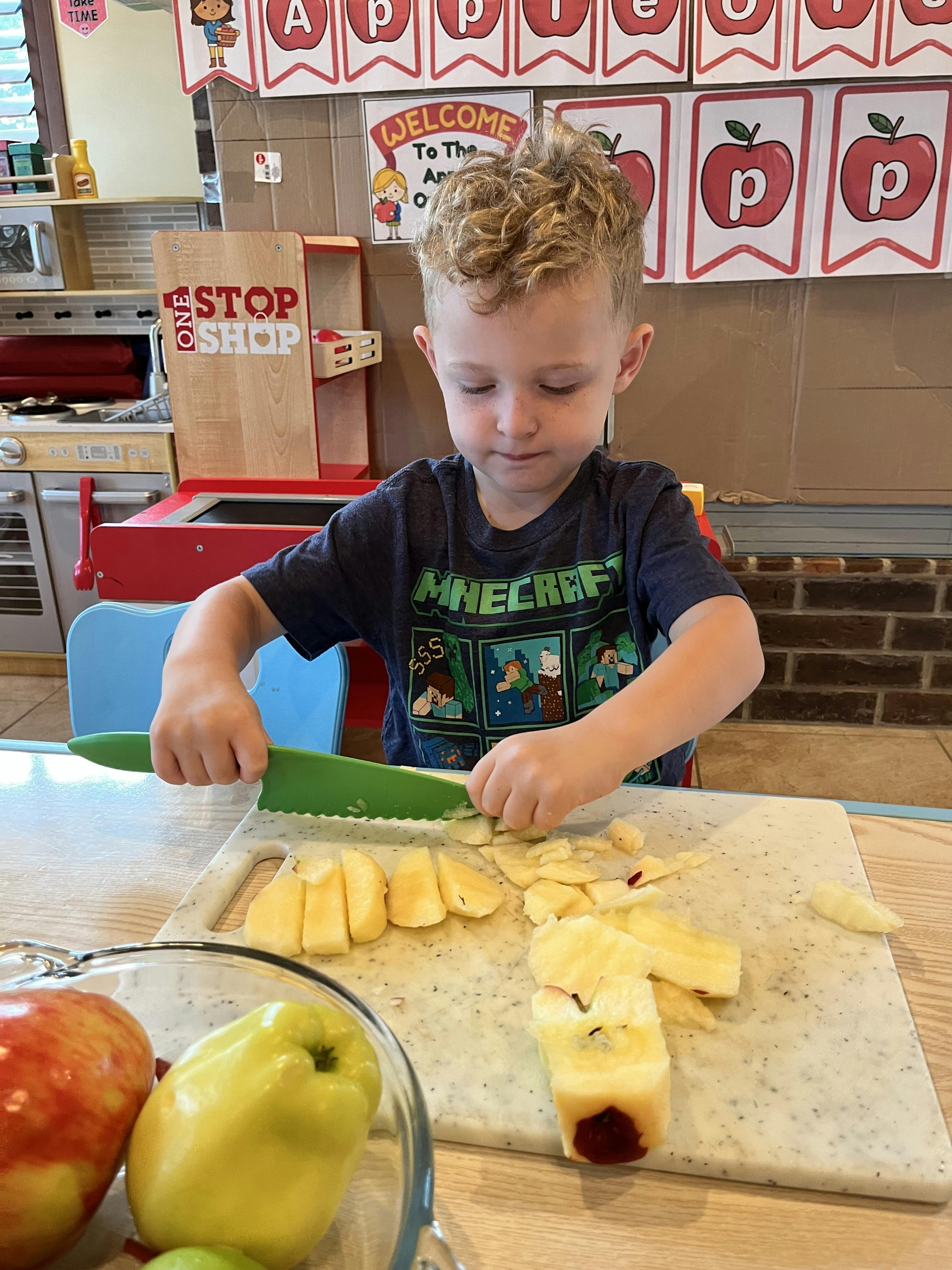Child cutting apples with a green knife on a cutting board