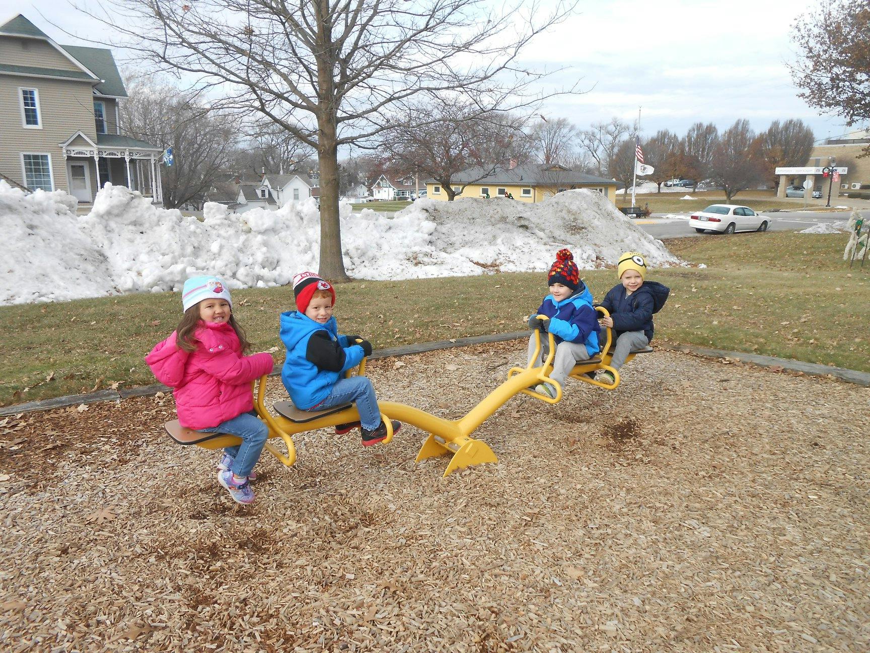 Four children on a yellow seesaw in a playground
