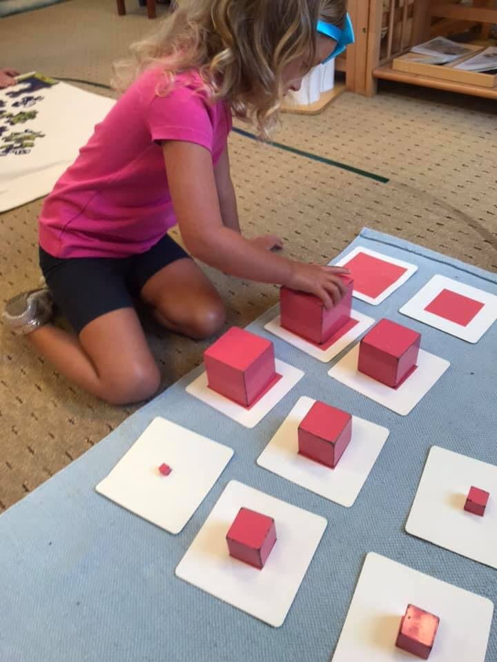 Child kneeling and placing a red block on a white card