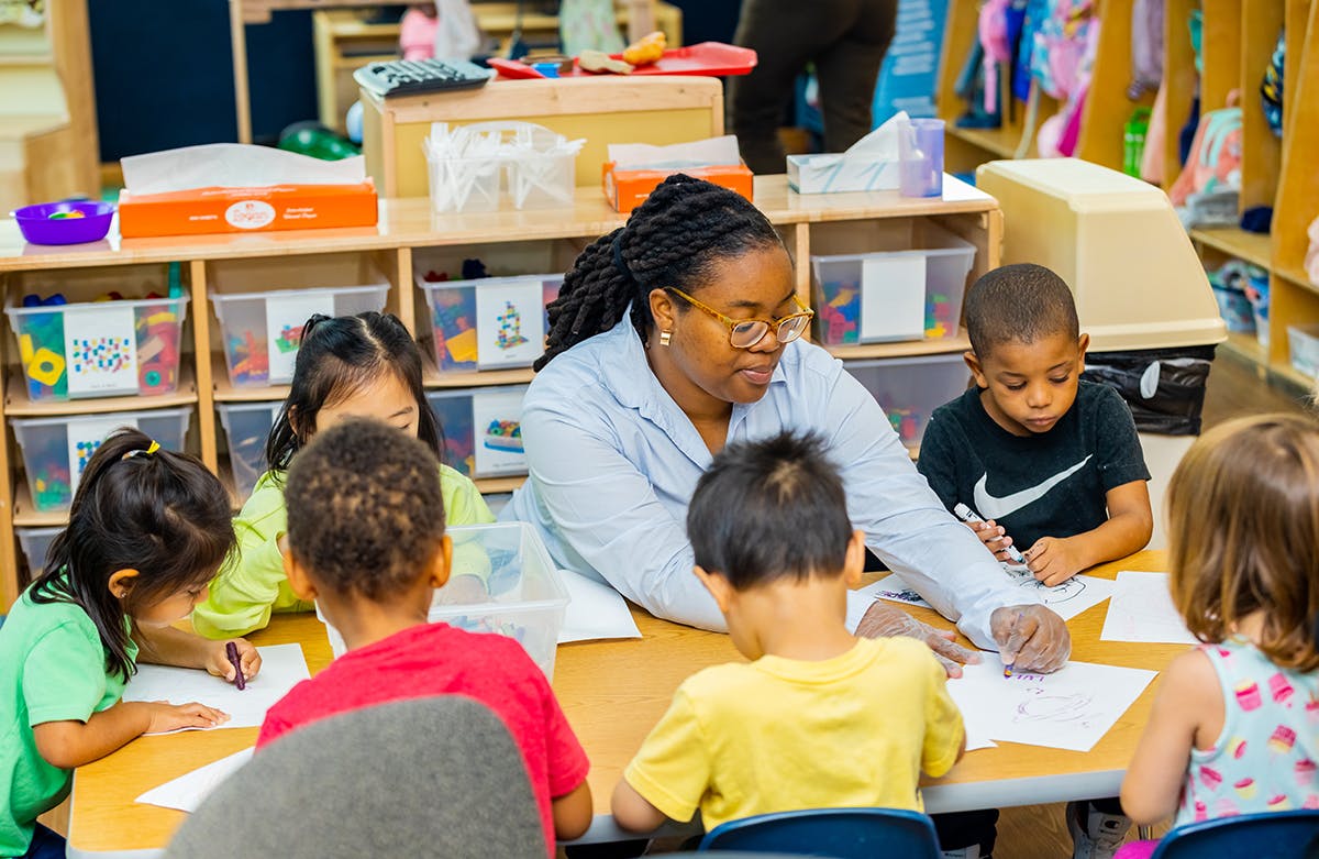 Adult and multiple children drawing at a table in a classroom