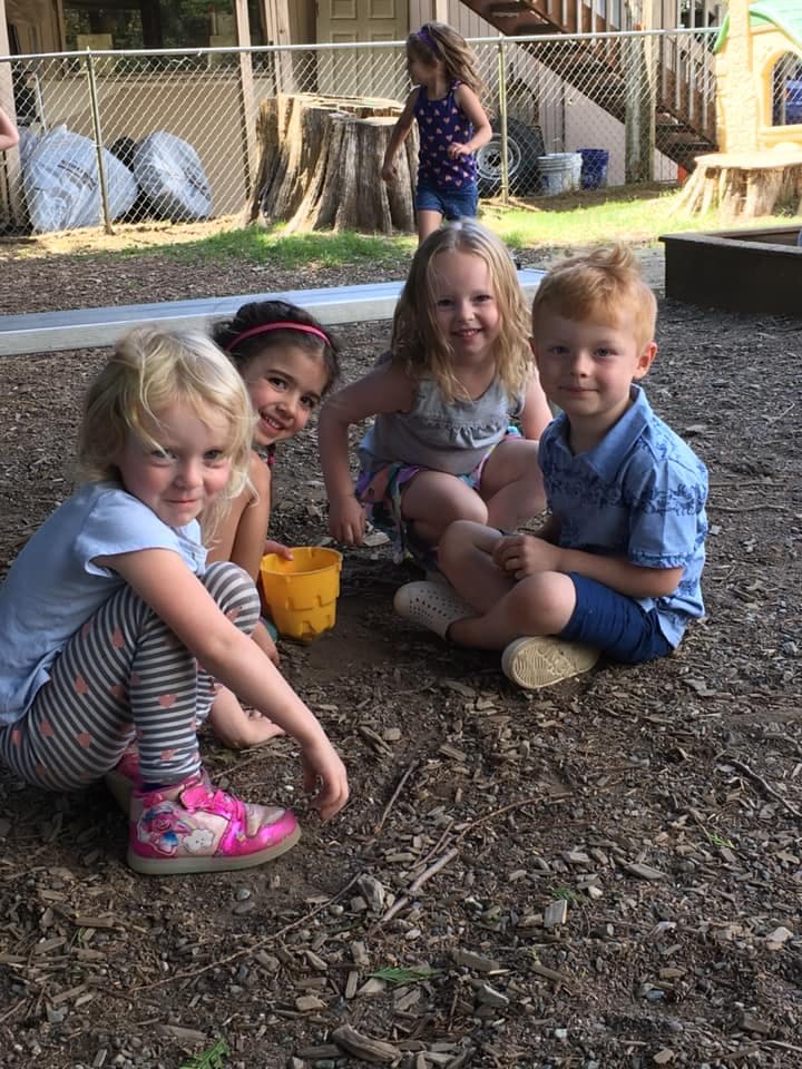Four children sitting on the ground, one child standing in the background