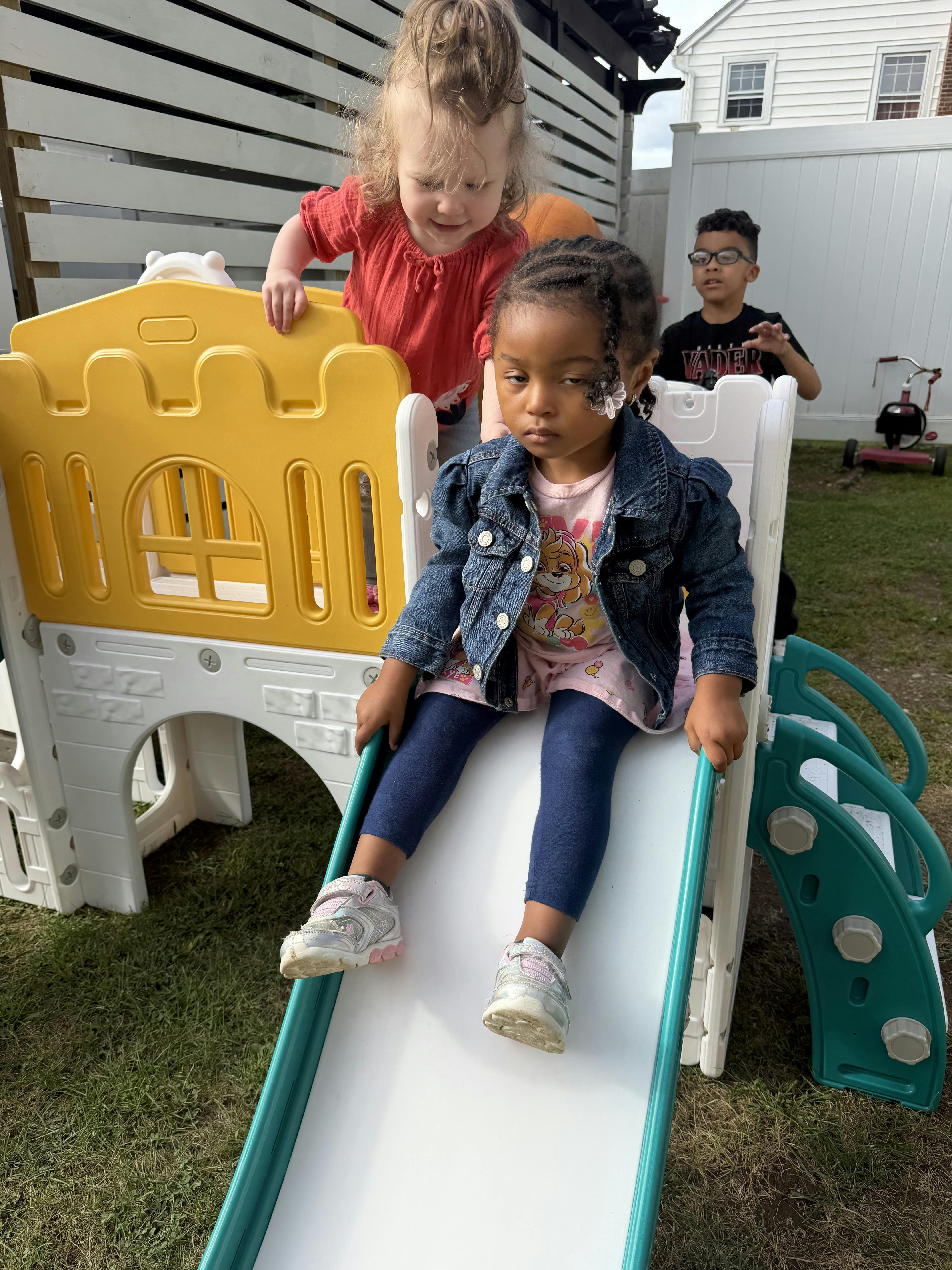 Three children playing on a plastic slide and play set in a backyard