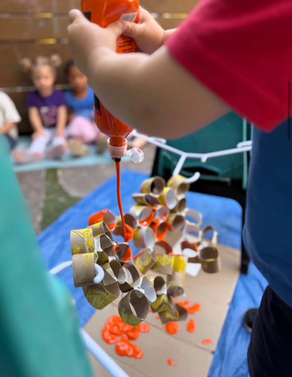 Person squeezing orange paint onto a craft made of cardboard tubes