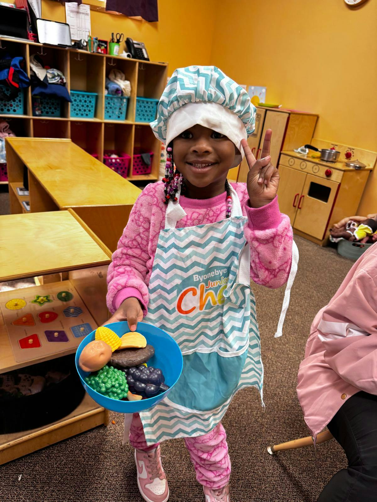 Child in a chef's hat and apron holding a bowl of toy food