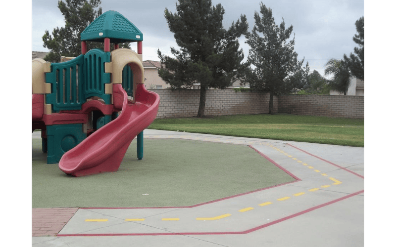 Playground structure with a red slide and a painted road on the ground